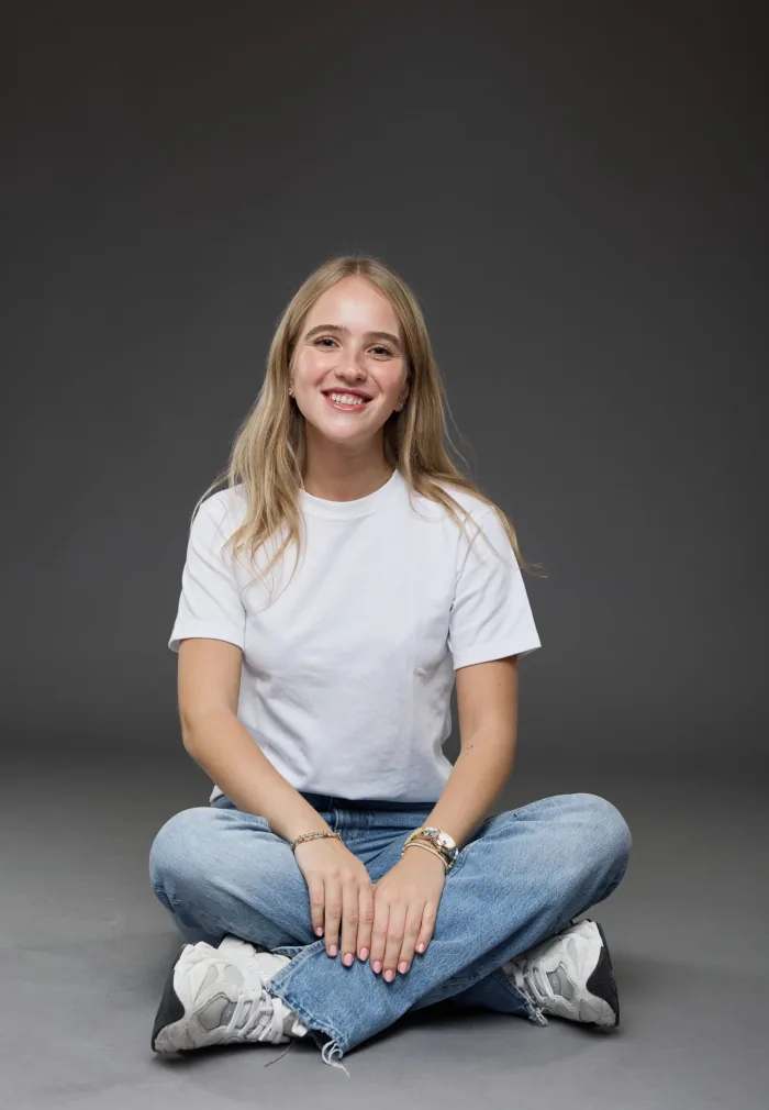 Portrait of Laura Schulmann sitting cross-legged in a white T-shirt and jeans, smiling at the camera